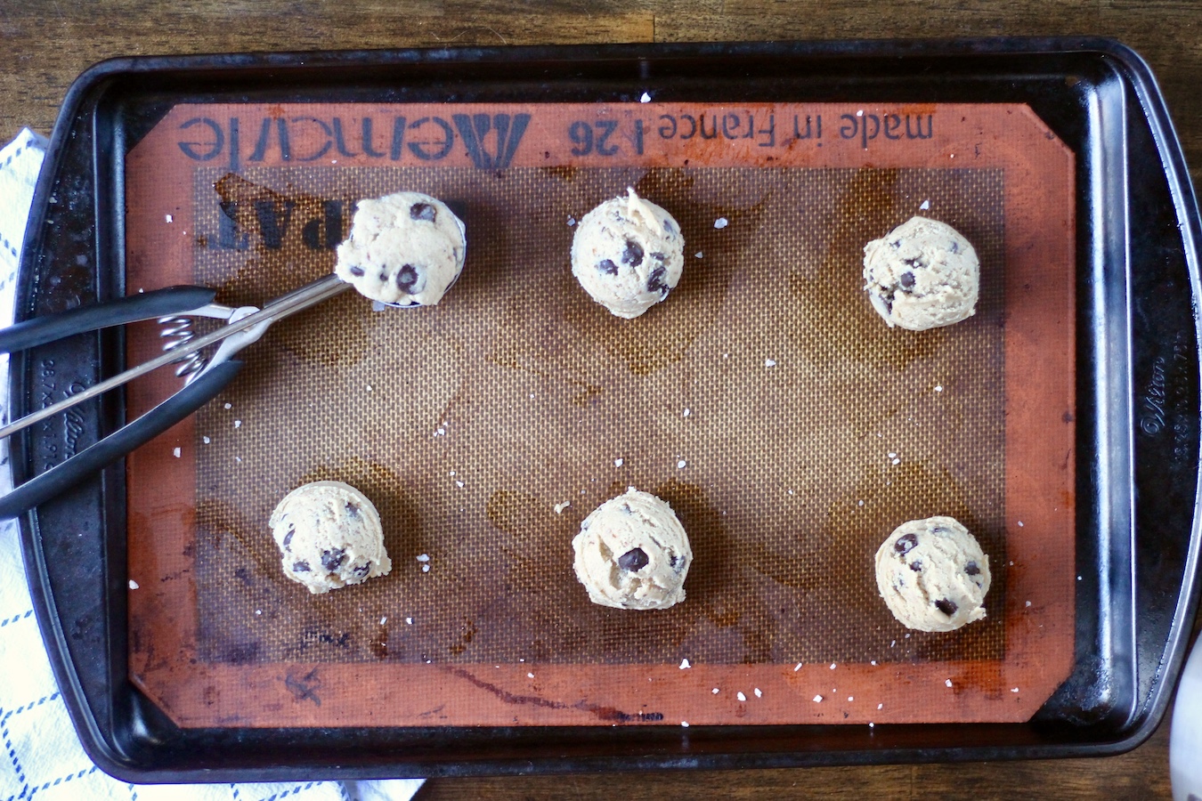 Six egg free chocolate chip cookie dough balls on a lined cookie sheet.