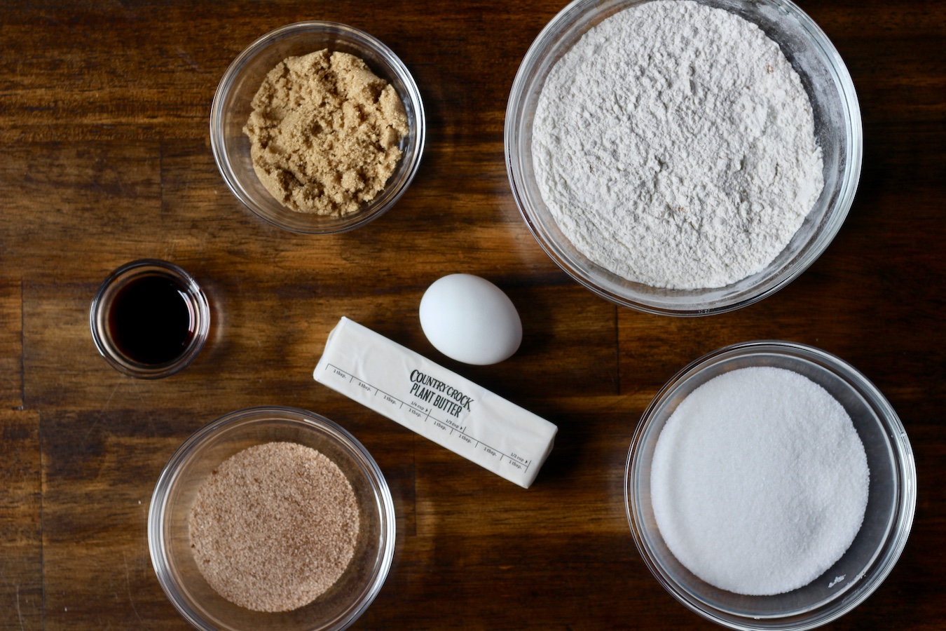 Ingredients for snickerdoodles in glass bowls on a wooden table.