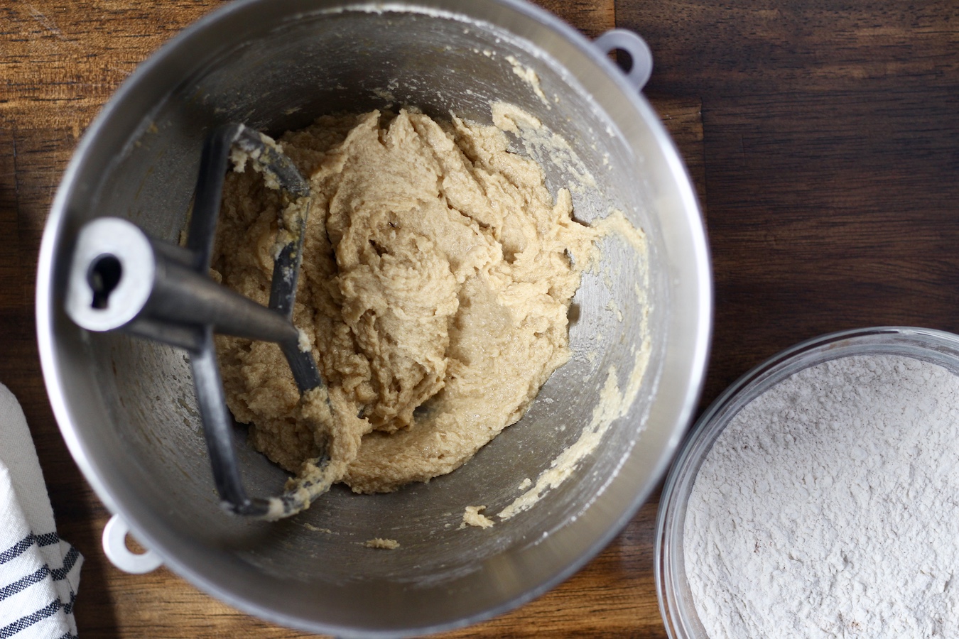 The stand mixer bowl with batter and a glass bowl to the right with the flour mixture.