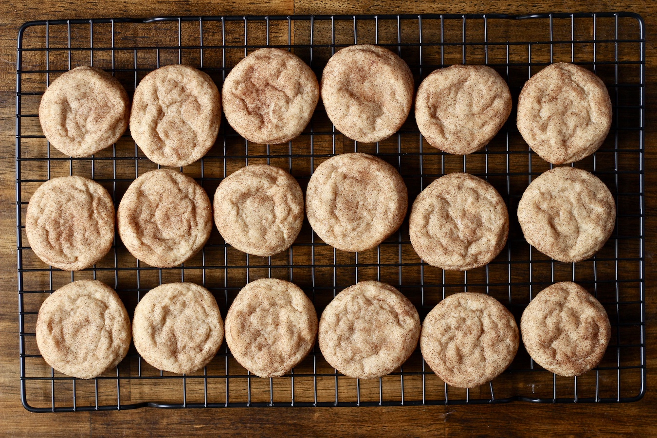Baked snickerdoodle cookies on a cooling rack on a wooden table.