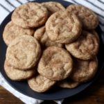 A blue plate piled with snickerdoodle cookies on a white and blue striped dish towel.