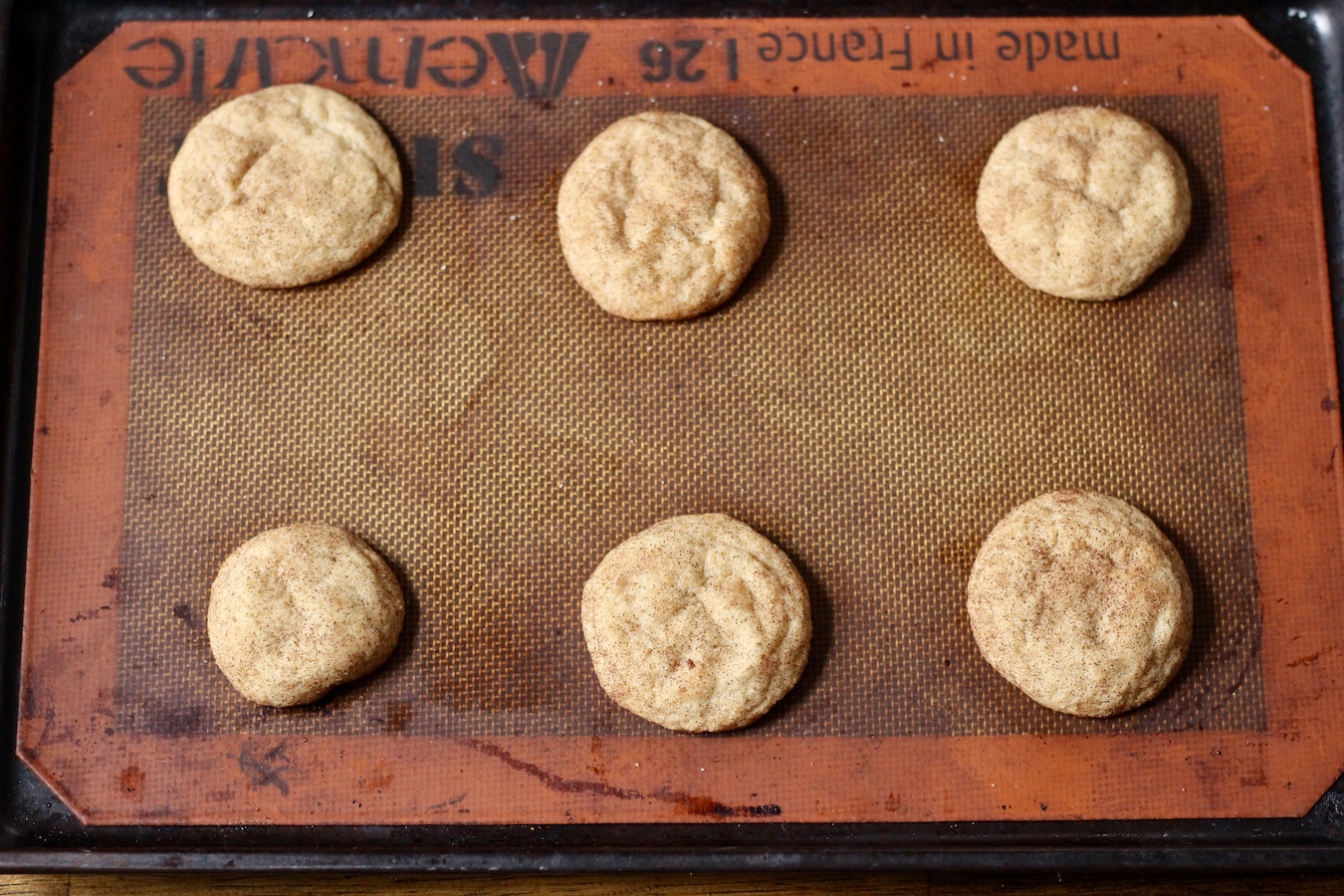 six baked snickerdoodle cookies on a cookie sheet.