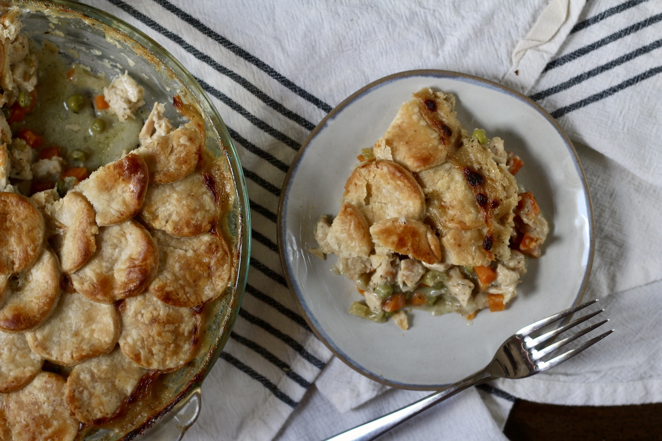A slice of chicken pot pie on a small plate on the right and a pan of chicken pot pie on the left.