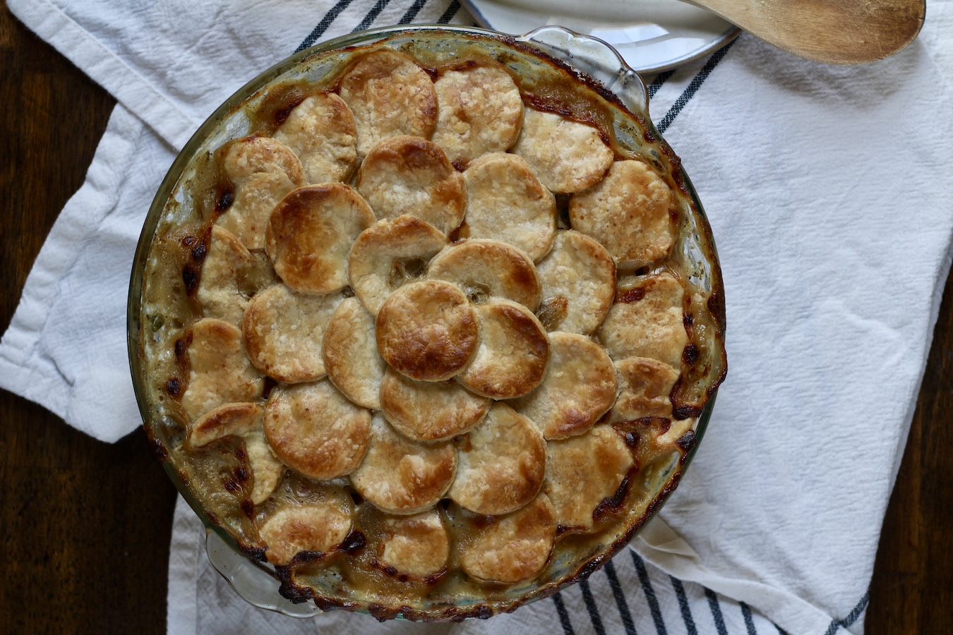 Baked chicken pot pie in a pie pan on a white and blue striped dish towel.