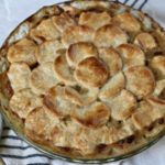 Baked chicken pot pie with a wooden spoon to the left and a white and blue striped dish towel on the bottom.