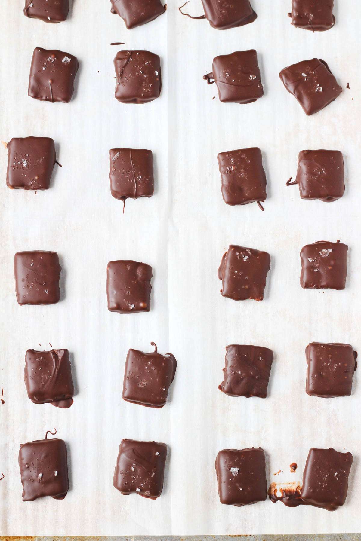 A white parchment paper with dark chocolate dipped graham crackers sprinkled with sea salt after the chocolate has set.