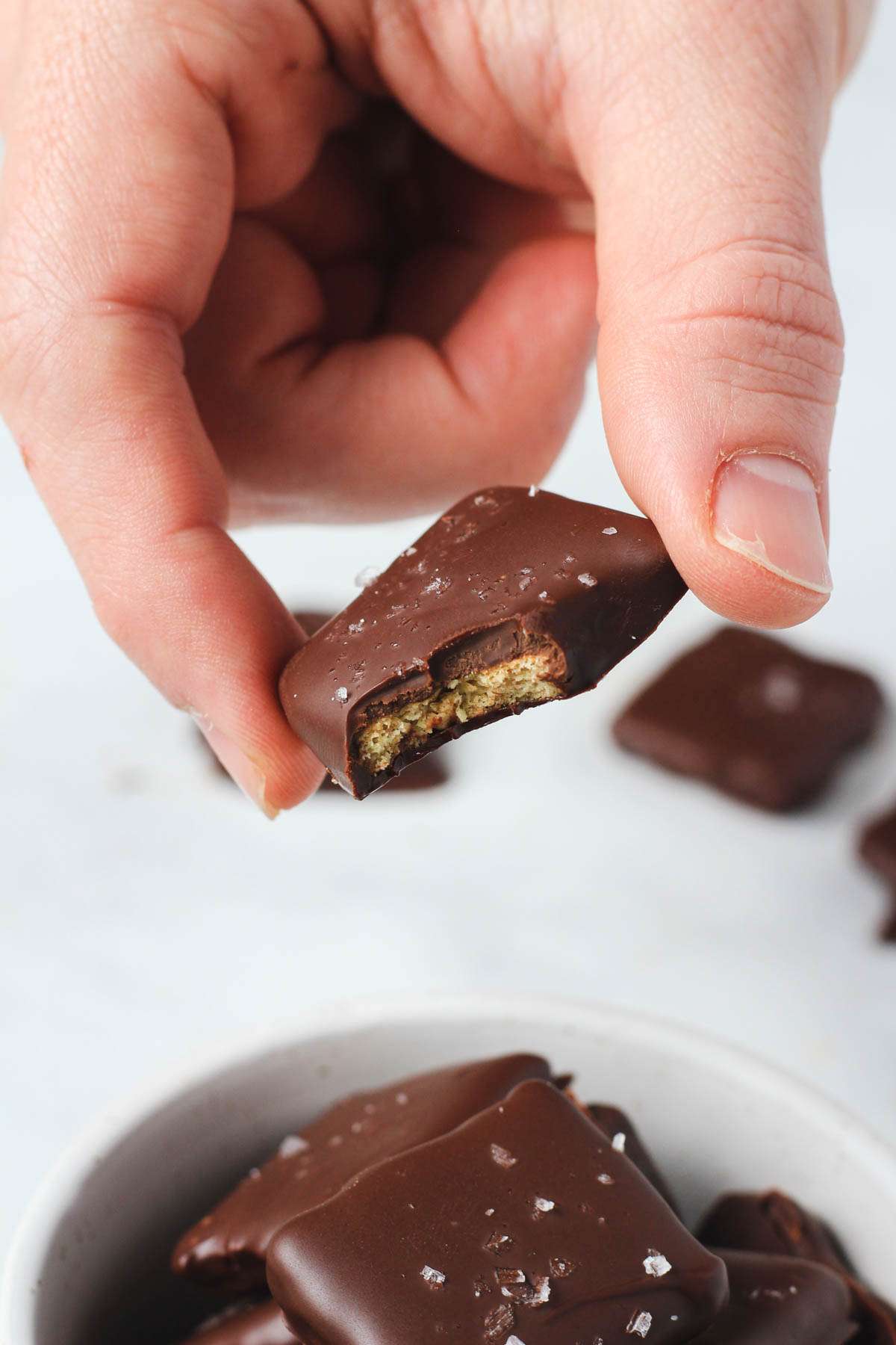 A hand holding a chocolate dipped graham cracker with a bite taken out.