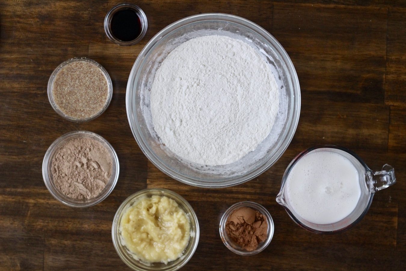Many glass bowls with the different ingredients on a wooden table.