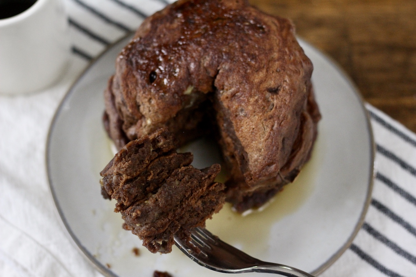Stack of Chocolate Protein Pancakes with a fork with a bite on them on a plate on a dish towel.