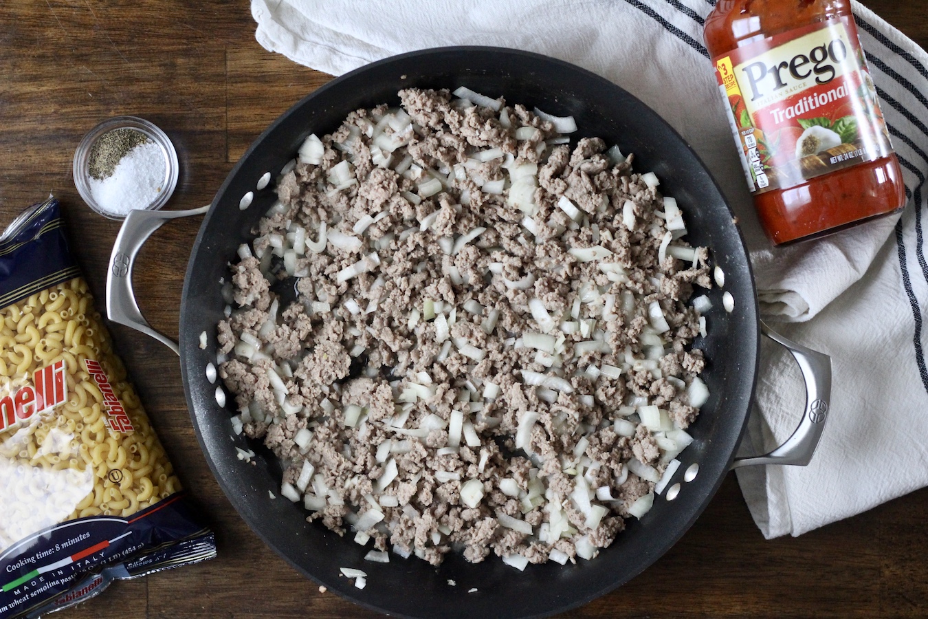 Browned meat in a skillet with a bag of pasta to the left and a jar of sauce to the right.