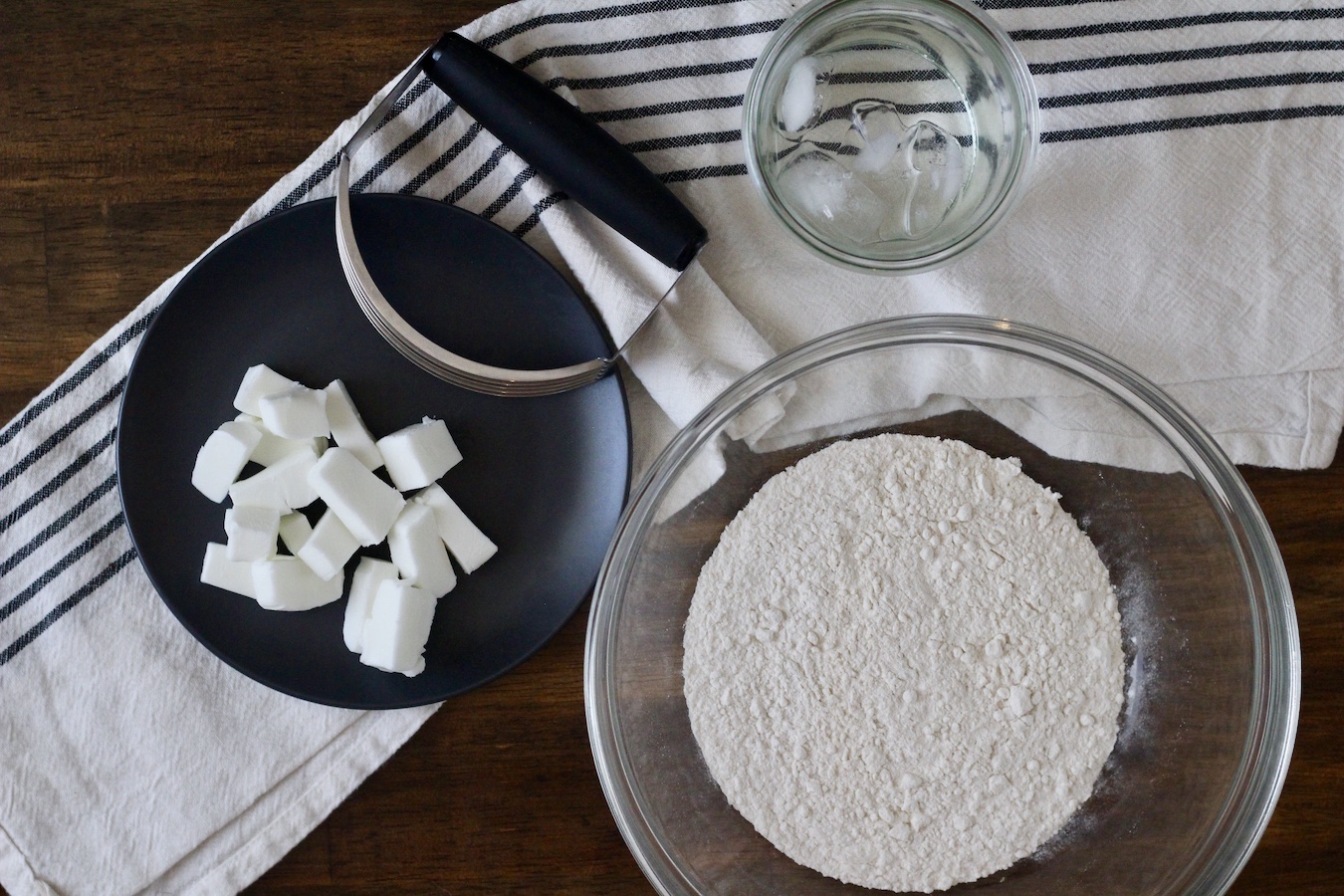 Flour, water, and crisco in glass bowls with a pastry cutter.