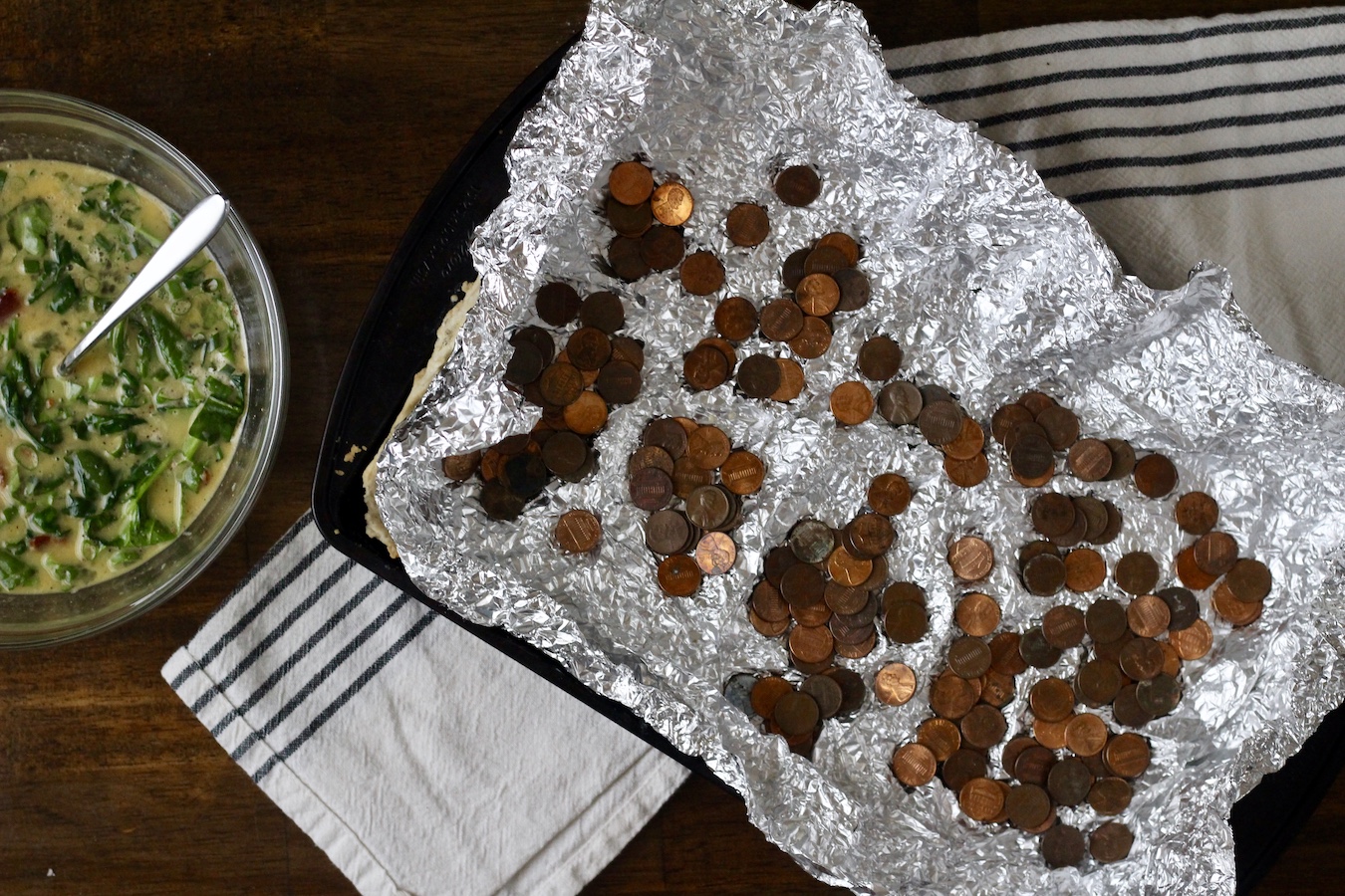 The slab quiche pie crust with the pie weights and a bowl with the egg mixture.