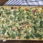 Baked slab quiche on a cooling rack with a blue and white dish towel.