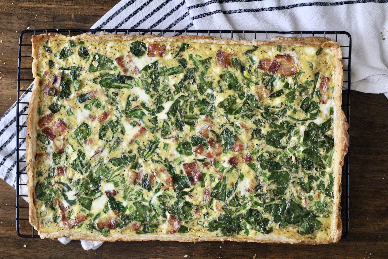Baked slab quiche on a cooling rack with a blue and white dish towel.