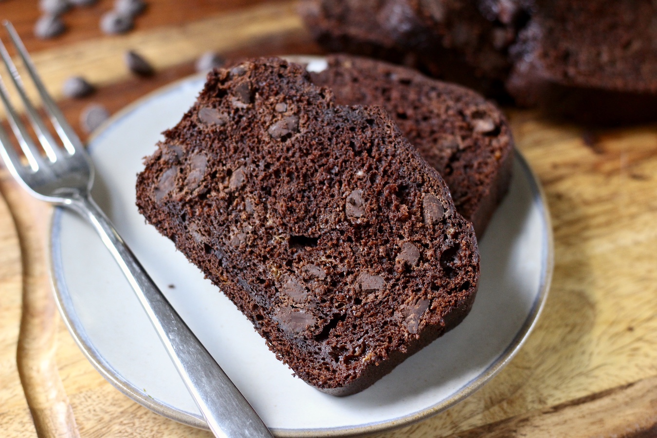 Two slices of banana bread on a small grey plate with a fork on a wooden cutting board.