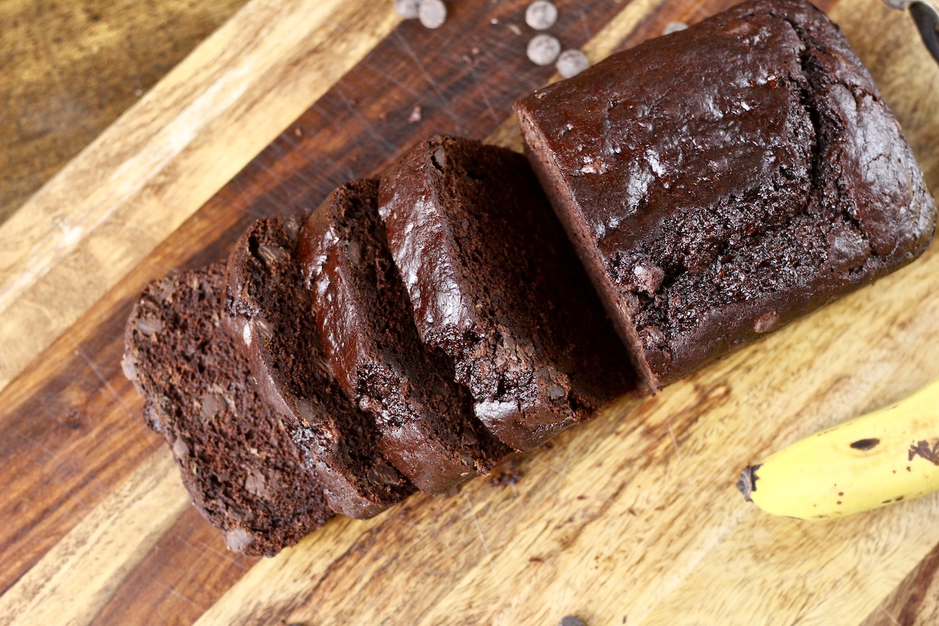 Sliced chocolate chip banana bread on a wooden cutting board with a banana on the right.