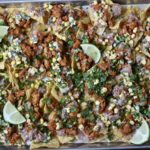 Loaded nachos on a sheet pan topped with lime wedges.