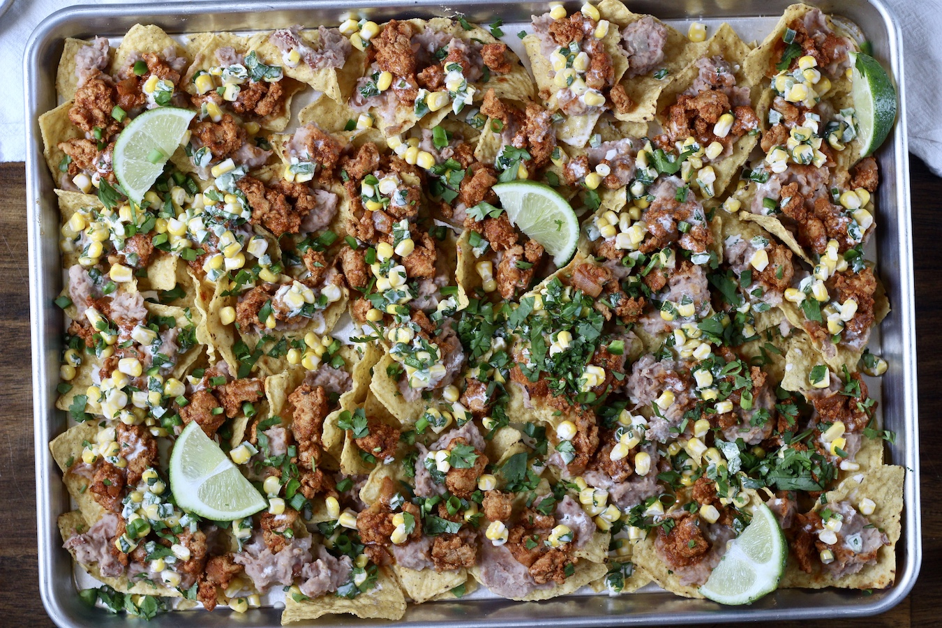 Loaded nachos on a sheet pan topped with lime wedges.