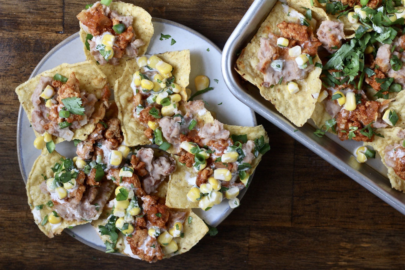 A plate of loaded nachos with a sheet pan of loaded nachos to the left.