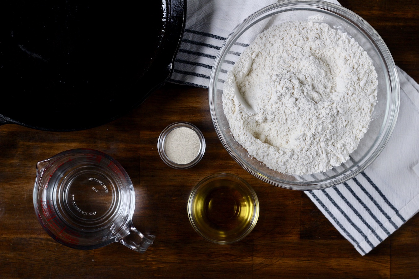 Ingredients in glass bowls on a wooden counter with a cast iron skillet to the left.