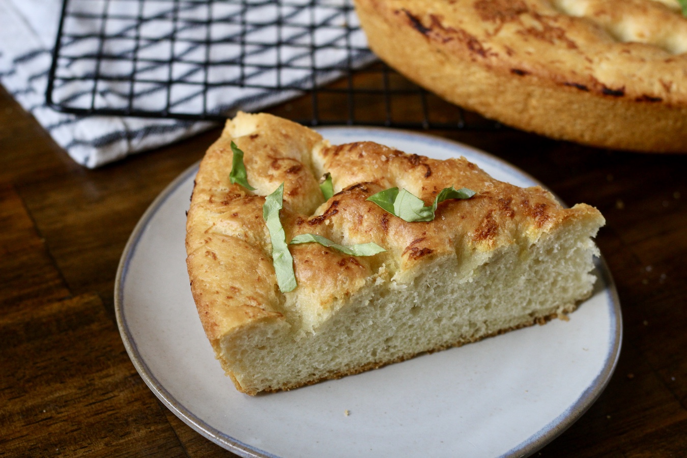A slice of skillet focaccia on a grey plate with chopped basil on top.