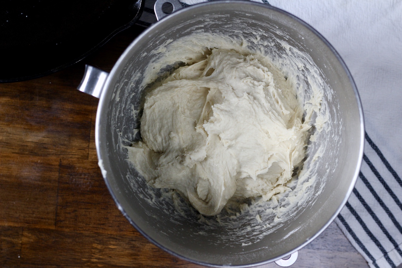 Focaccia dough in a silver mixing bowl on a wooden counter.
