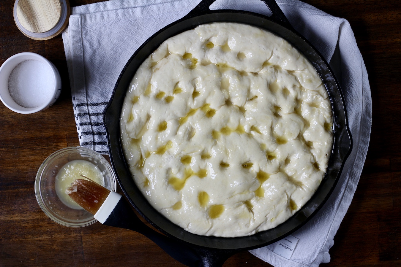 Skillet garlic focaccia in a cast iron skillet with holes, olive oil, and garlic butter brushed on top.