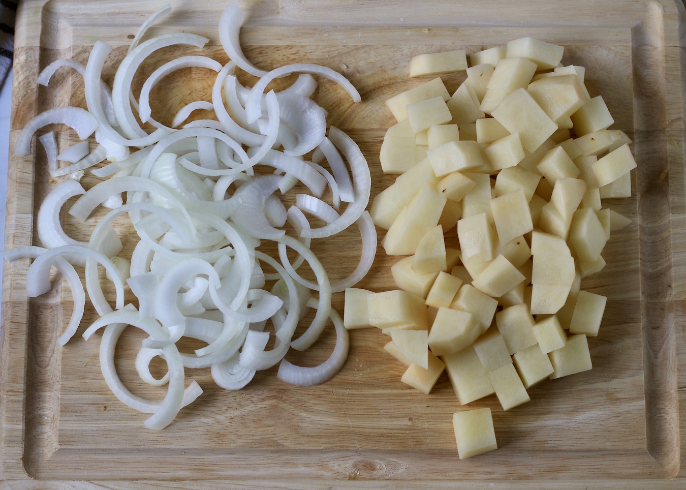 Sliced onion and diced potatoes on a wooden cutting board.