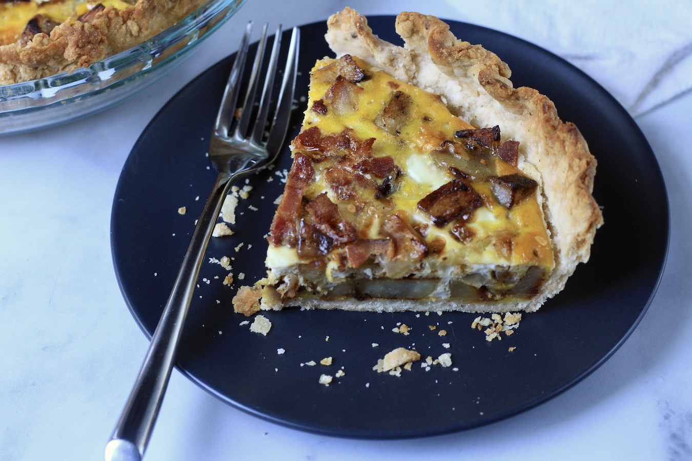 A slice of bacon and potato quiche on a blue plate looking from the side.