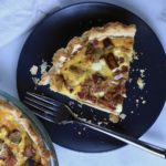 A slice of bacon and potato quiche on a blue plate with a for.