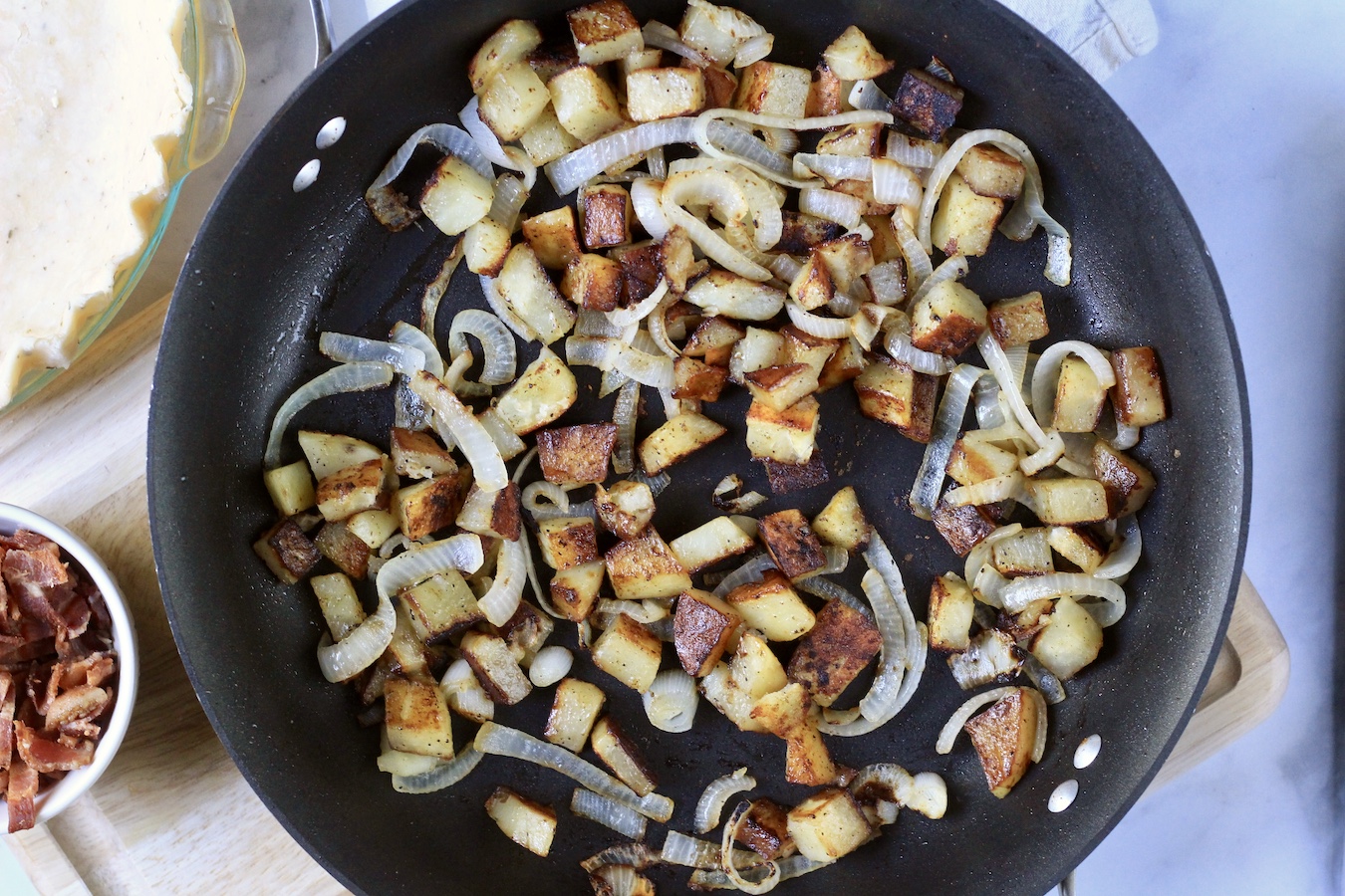 A skillet with bacon and onion cooking.