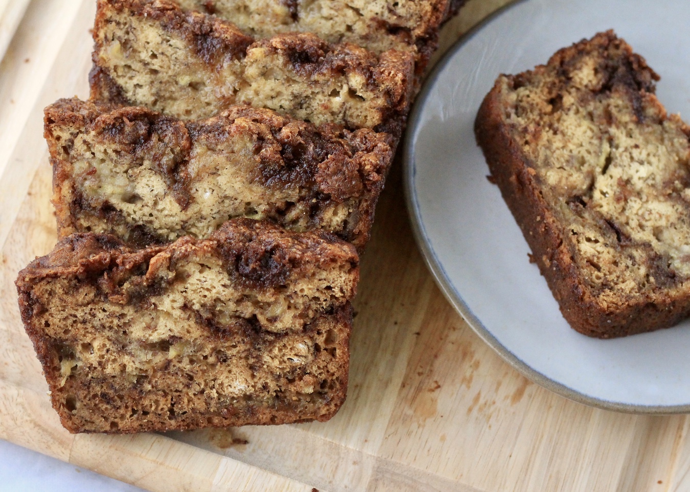 Slices of banana bread on a wooden cutting board with a slice on a small plate.