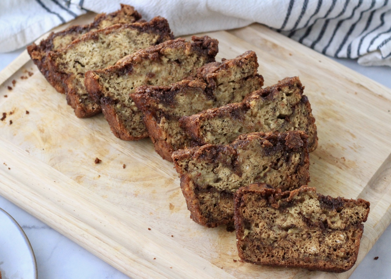 Sliced cinnamon swirl banana bread on a wooden cutting board.