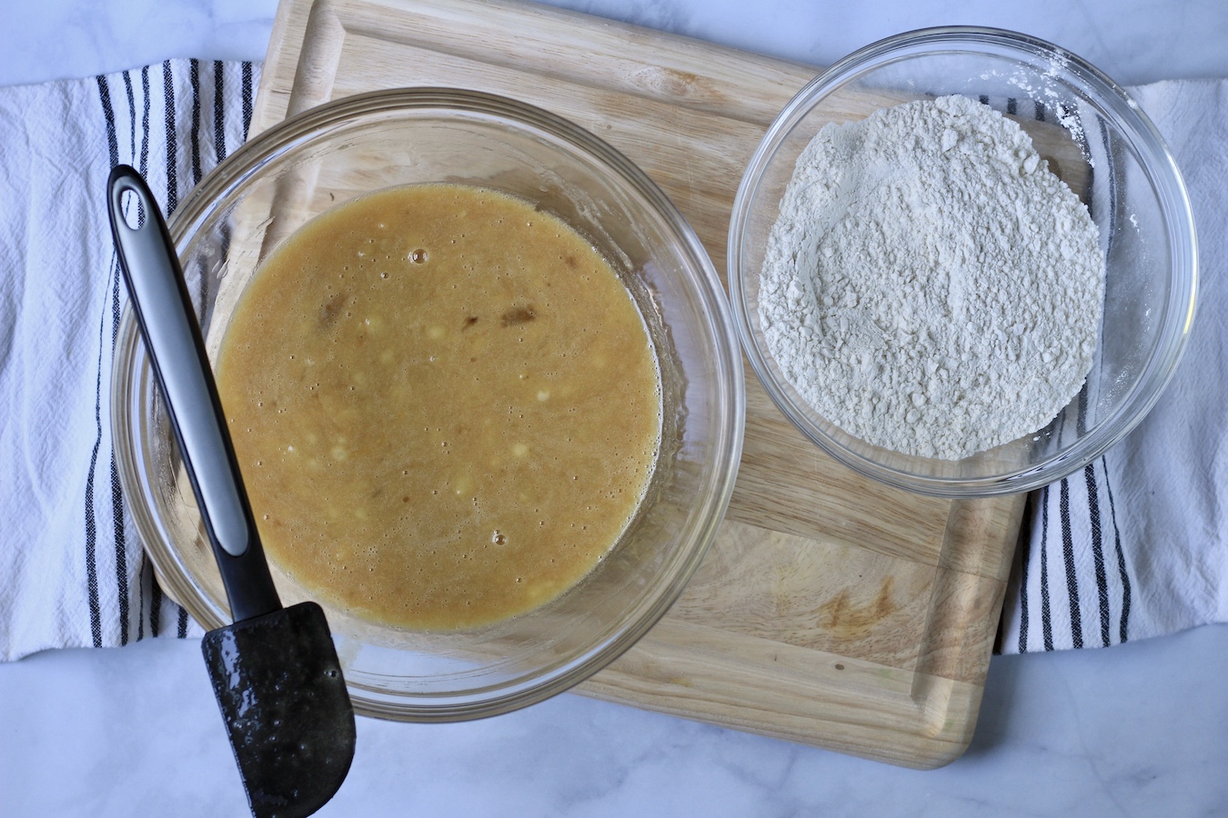 A large bowl with liquid ingredients and another bowl with dry ingredients on a wooden cutting board.
