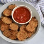 A white bowl filled with zucchini bites in the front and a small bowl of marinara in the back.