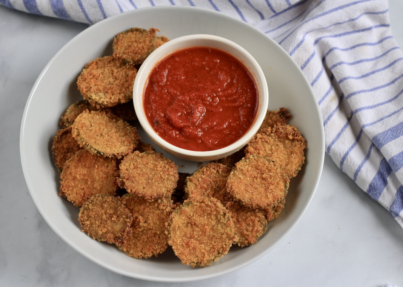 A white bowl filled with zucchini bites in the front and a small bowl of marinara in the back.