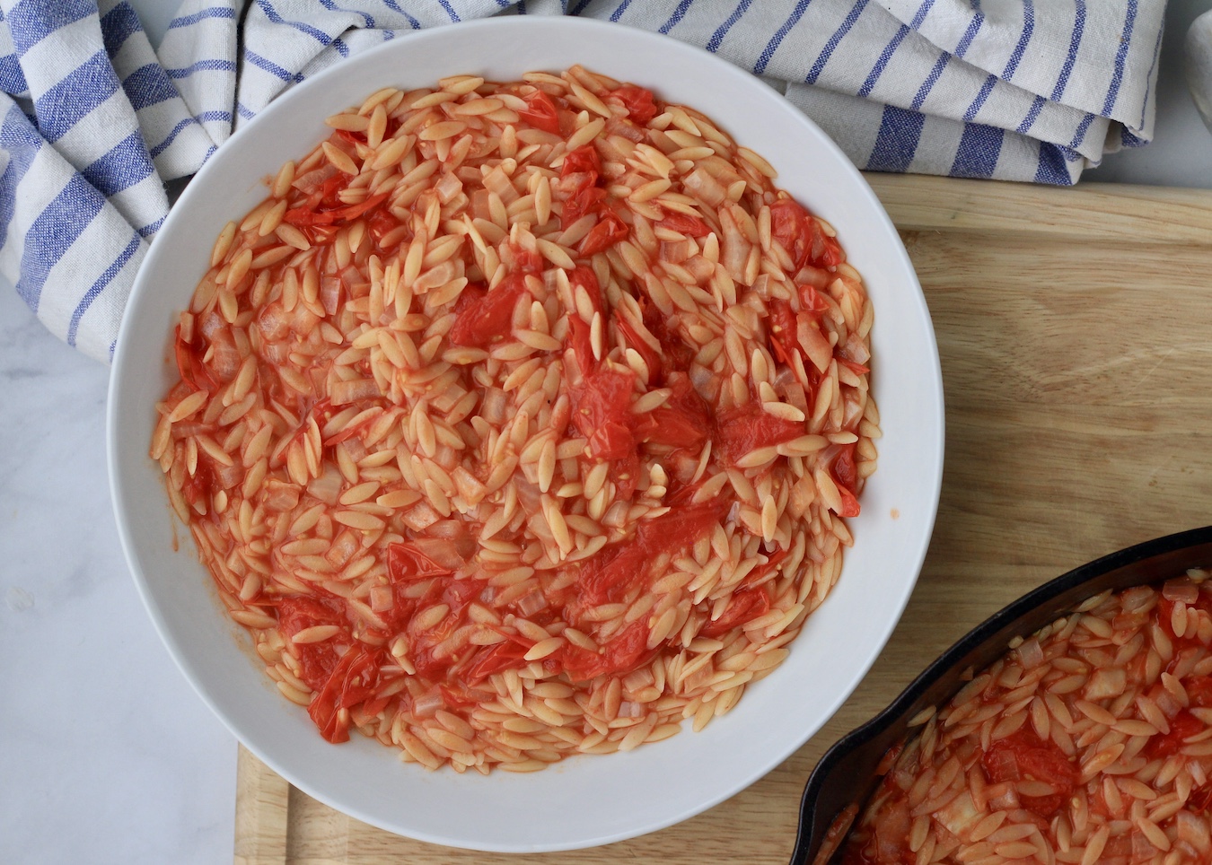A large white bowl with roasted tomato orzo on a wooden cutting board.
