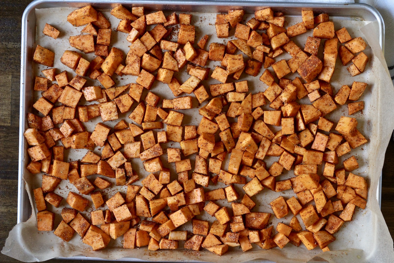 A sheet pan with sweet potatoes coated in seasoning.