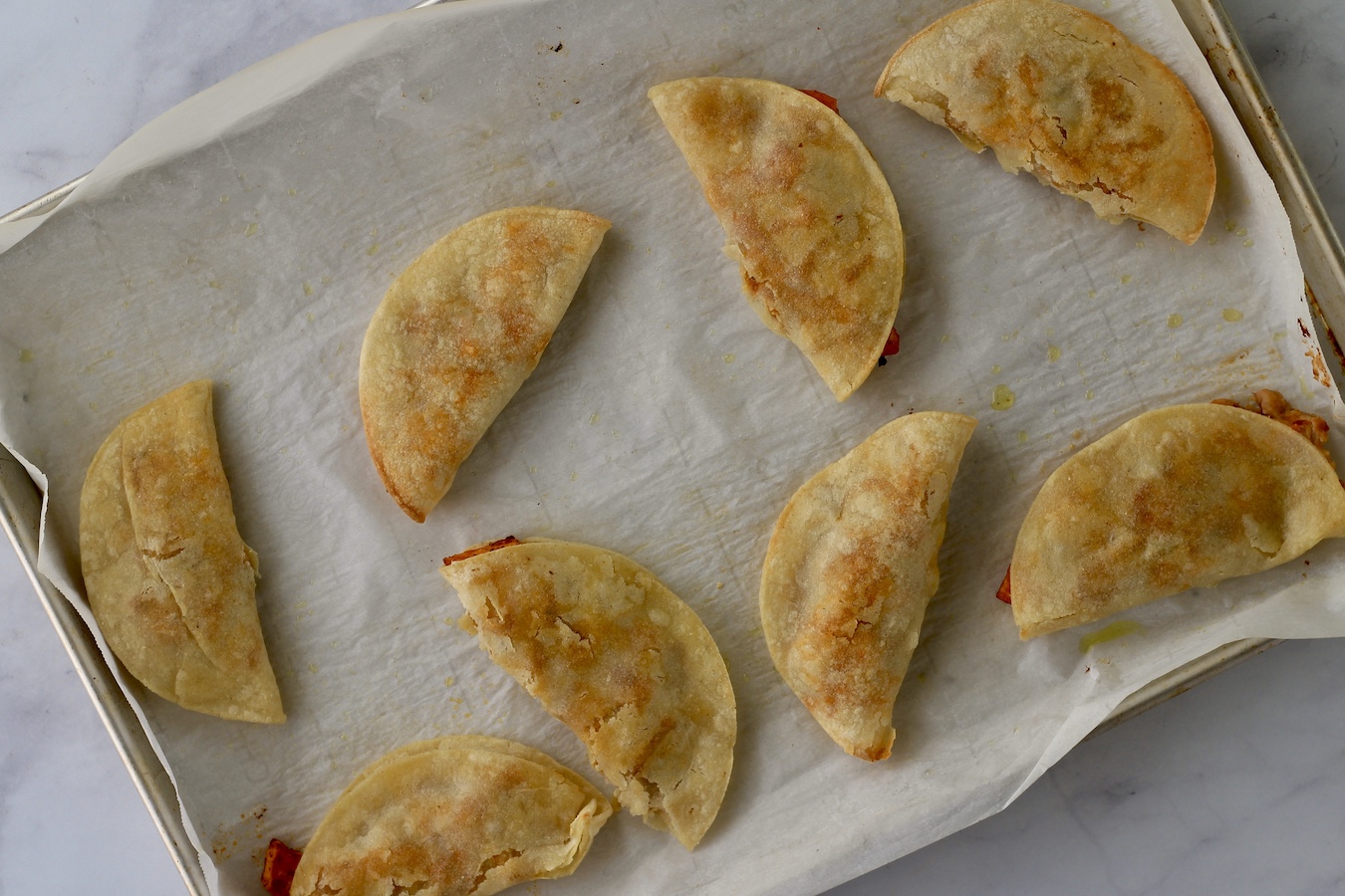 A sheet pan covered with parchment paper and 8 crispy sweet potato tacos.