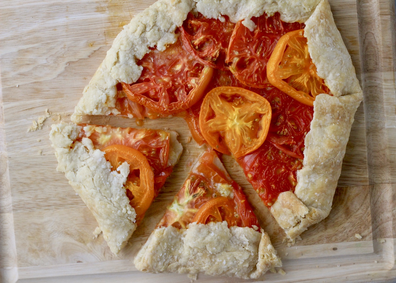 A wooden cutting board with heirloom tomato galette, two slices cut out at the bottom.