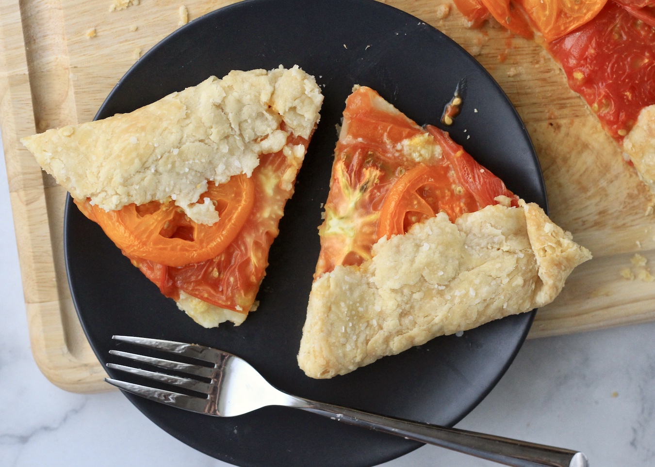 Two slices of heirloom tomato galette on a blue plate with a fork on a wooden cutting board.