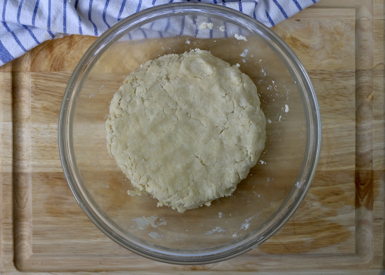 A large bowl with pastry dough in a flat disk on a wooden cutting board.