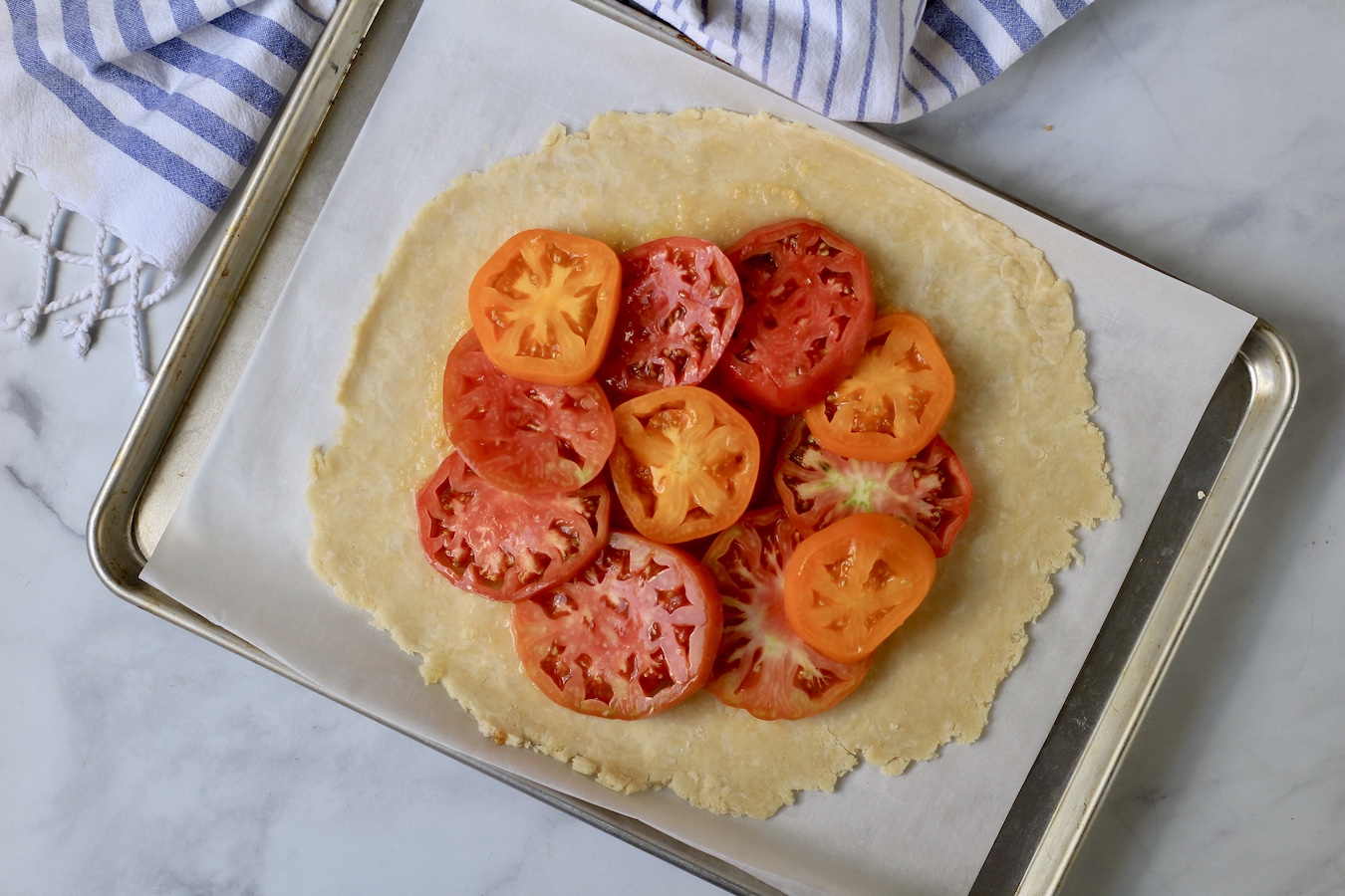 Tomatoes layered on a rolled out pastry dough on a parchment paper on a sheet pan.