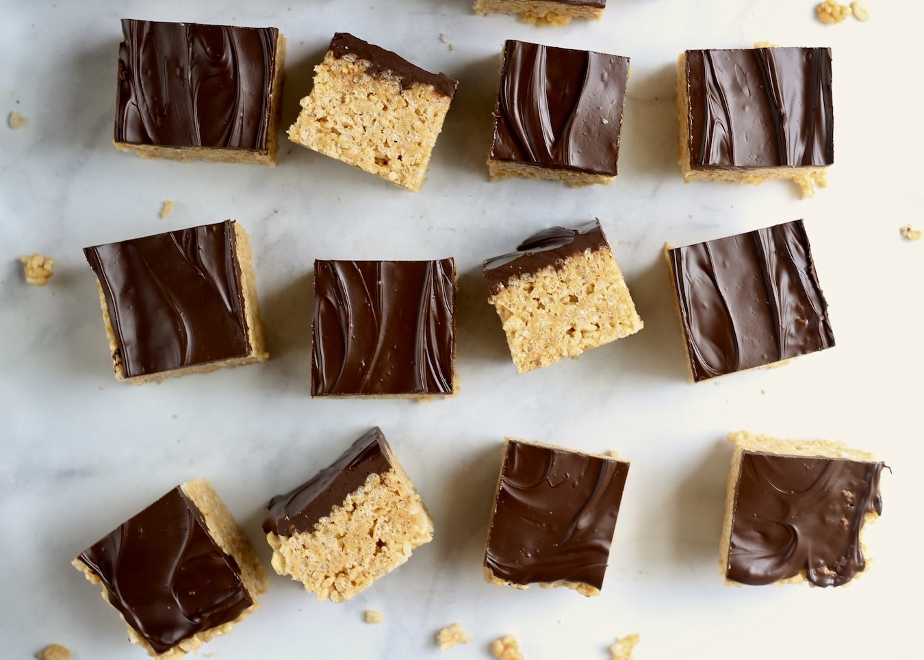 Twelve cut peanut butter rice krispie treats in 3 rows of 4 with one rice krispie turned on the side in each row to show the layer of chocolate with a peanut butter rice krispie base.