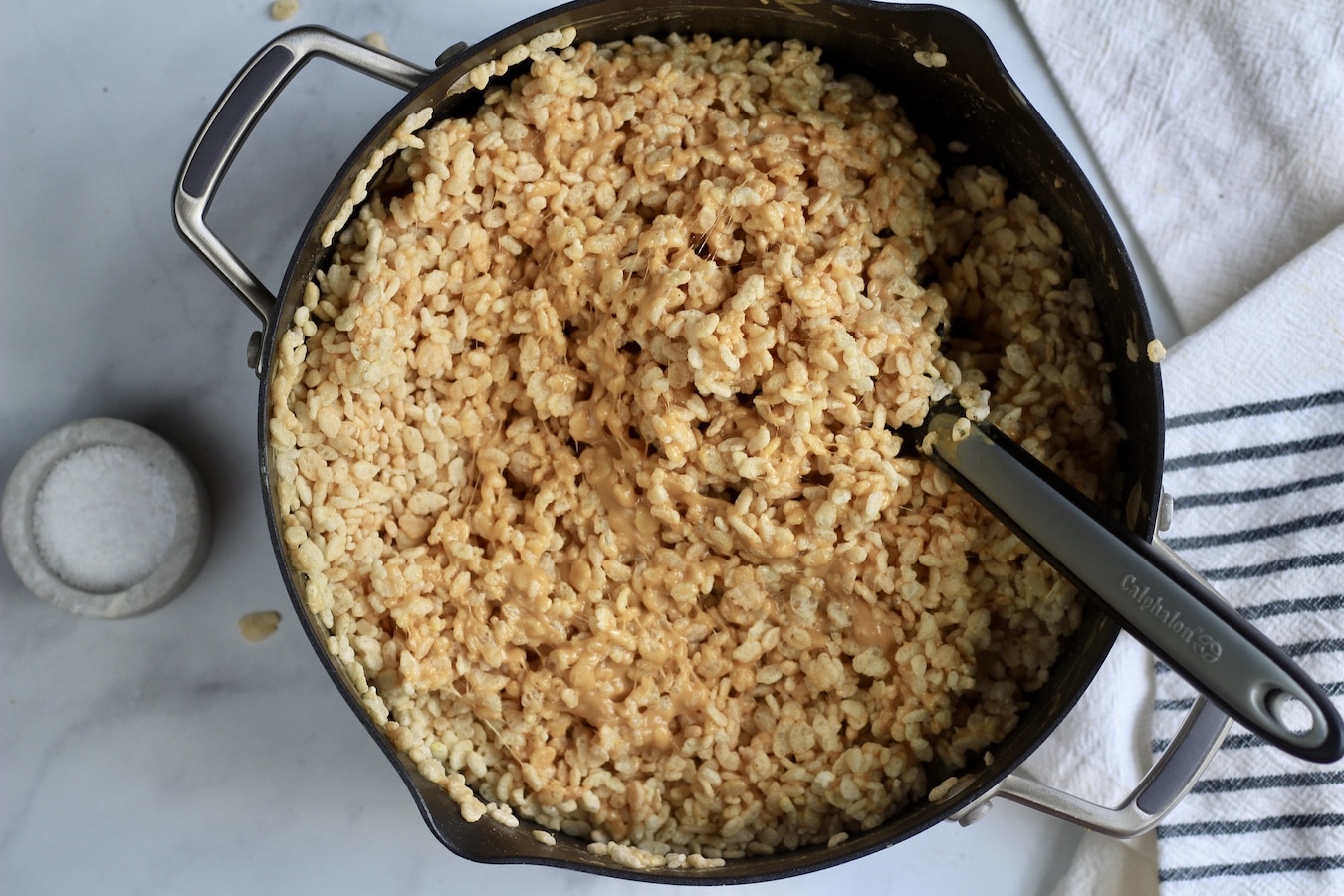 Peanut butter rice kirspies in a non-stick pan with a spatula next to a stone bowl with salt.