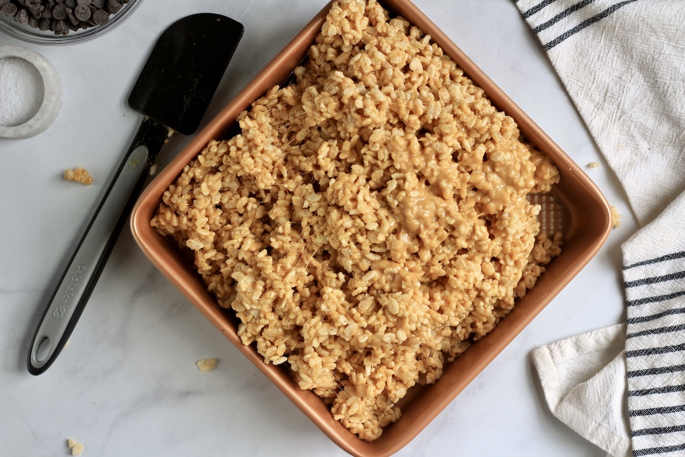 Peanut butter rice krispies poured into a non-stick pan with a black rubber spatula to the left.