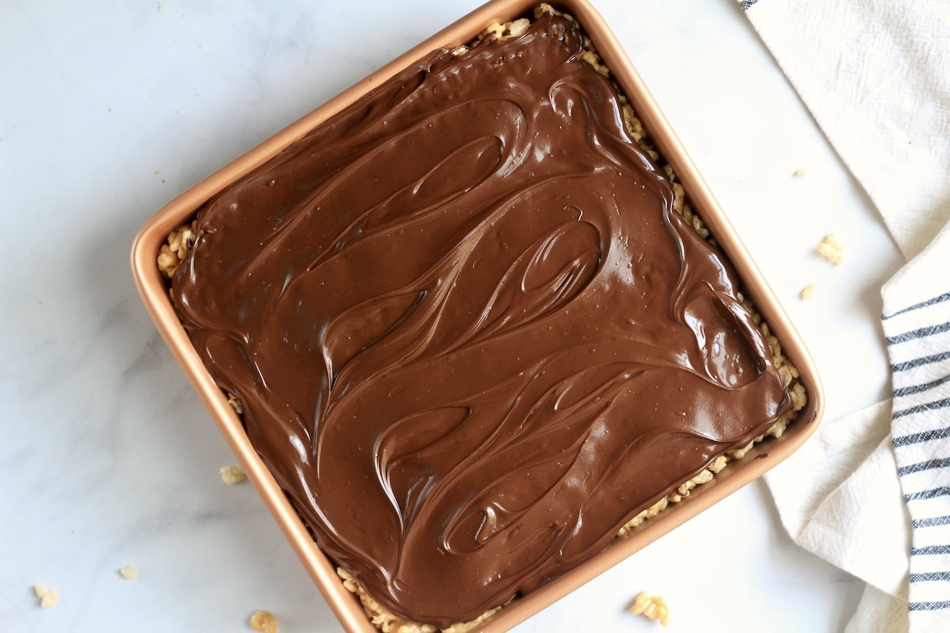 Chocolate coated peanut butter rice krispie treats in a copper pan on a marble counter.