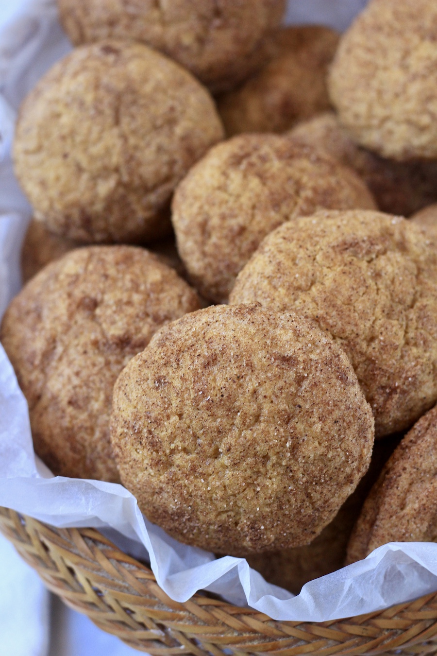 A woven basket with parchment paper filled with pumpkin spice snickerdoodles.
