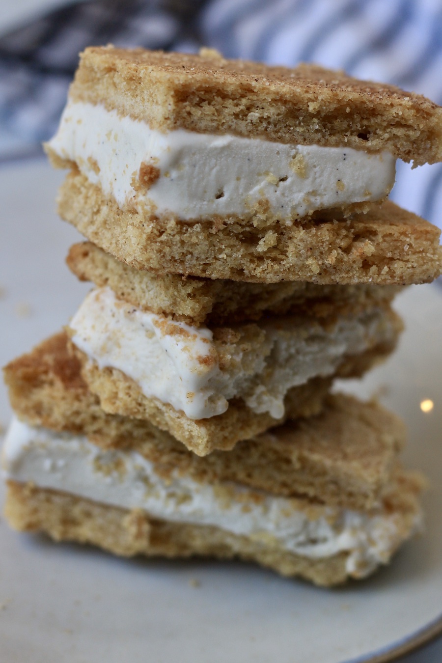A stack of 3 ice cream sandwiches on a plate with a blue and white dish towel in the back.