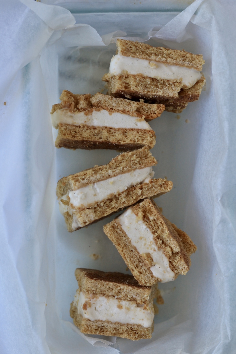 A parchment paper inside a baking dish with 5 ice cream sandwiches on their side.